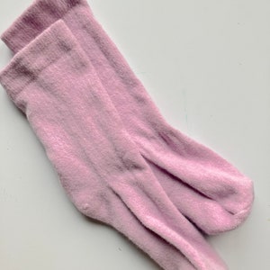 Può includere: Un paio di calzini morbidi e rosa in materiale peloso. I calzini sono piegati insieme e pronti per essere indossati.