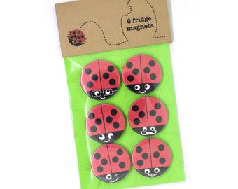 May include: Six red ladybug fridge magnets with black spots and different facial expressions. The magnets are packaged on a green background with the text "6 fridge magnets" on a brown background.