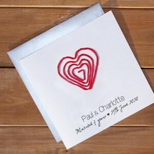 May include: A white card with a red heart made of yarn. The card says "Paul & Charlotte Married 7 years 29th June 2020".