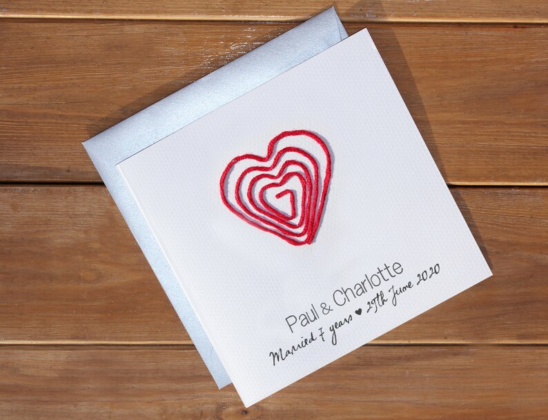 May include: A white card with a red heart made of yarn. The card says "Paul & Charlotte Married 7 years 29th June 2020".