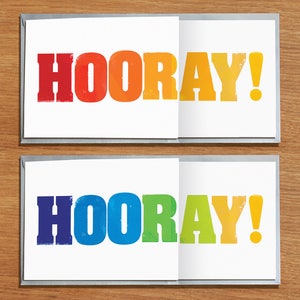 May include: Two white cards with the word "HOORAY!" printed in rainbow colours. The top card has red, orange, yellow, and green letters. The bottom card has blue, green, yellow, and orange letters.