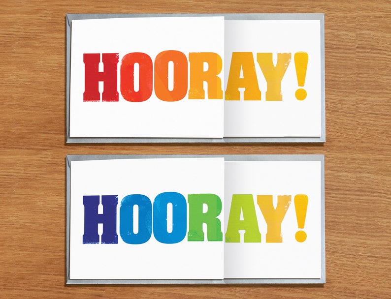 May include: Two white cards with the word "HOORAY!" printed in rainbow colours. The top card has red, orange, yellow, and green letters. The bottom card has blue, green, yellow, and orange letters.