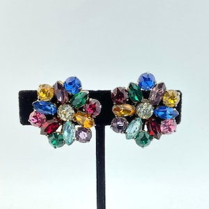 May include: A pair of cluster earrings featuring a central clear stone surrounded by a circular arrangement of multi-colored faceted marquise and round rhinestones in shades of blue, green, red, yellow, pink, and purple set in silver-tone metal.