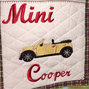 May include: A white quilted fabric square with red embroidered text "Mini Cooper" and an embroidered image of a yellow convertible car.