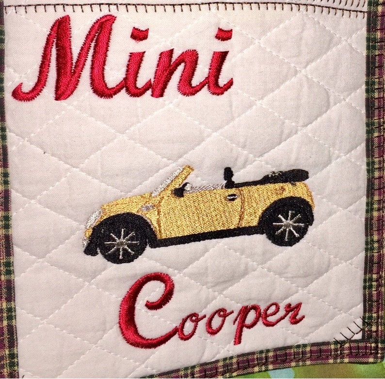 May include: A white quilted fabric square with red embroidered text "Mini Cooper" and an embroidered image of a yellow convertible car.