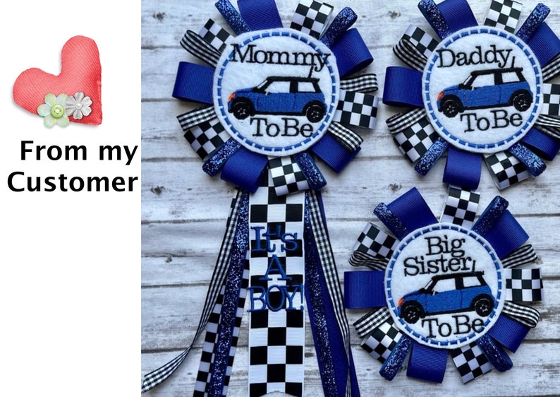 May include: Three blue and white checkered ribbon rosettes with a white circle in the center. The circles have blue embroidery that reads "Mommy To Be", "Daddy To Be", and "Big Sister To Be". Each circle also has a blue miniature car graphic.