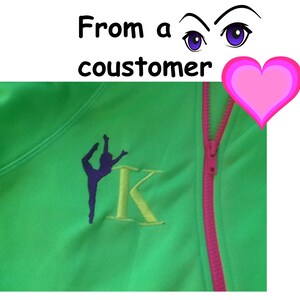 May include: Green zippered jacket with a pink zipper and a yellow embroidered letter K. A purple silhouette of a gymnast is embroidered next to the letter.