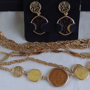 May include: A gold tone multi-strand necklace with amber and yellow glass pendant charms. The necklace is displayed with matching earrings with amber glass and gold tone filigree.