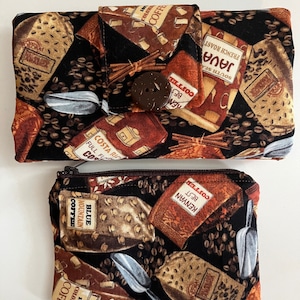 May include: A black fabric zippered pouch with a coffee bean pattern. The pouch has a brown button closure and a smaller zippered pouch attached to it. The smaller pouch has a zippered closure and a coffee bean pattern. The text on the pouches includes "Blue Mountain Coffee", "Kenyan Best Coffee", "Costa Rica Full Flavor Coffee", "South Sea Java French Roast", and "100% Colombian Coffee".
