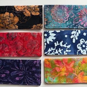 May include: Six fabric checkbook covers with floral patterns. The covers feature designs in black and gold, teal and pink, red, navy and white, purple and blue, and orange and green. Each cover is rectangular.