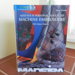 May include: Book cover with a blue and white checkered fabric with red and white embroidery. The book title is "Add Your Personal Touch to Machine Embroidery" with the subtitle "With Pattern Sheets". The book is published by Madeira.