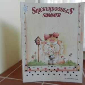 May include: A book cover with a whimsical illustration of a girl holding a bucket and a chick. The title is "Snickerdoodles Summer" by Christel  Winterberg.