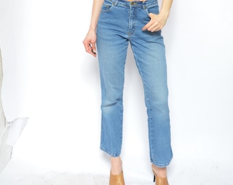 May include: A woman wearing a short-sleeved, orange, patterned shirt with a collar and blue jeans. She is wearing brown shoes.