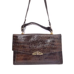 May include: A brown leather handbag with a crocodile pattern and a gold clasp. The bag has a shoulder strap.