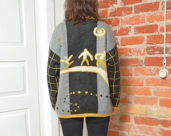 Può includere: Un maglione grigio, nero e giallo con un motivo geometrico e figure di persone che sciano. Il maglione ha un collo alto e maniche lunghe.