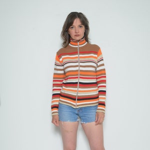 Puede incluir: Una mujer con un suéter a rayas con cremallera, pantalones cortos de mezclilla y botas de mezclilla.