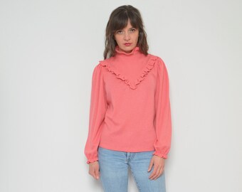 May include: A woman wearing a pink ruffled blouse with long sleeves and blue jeans. She is wearing brown ankle boots.