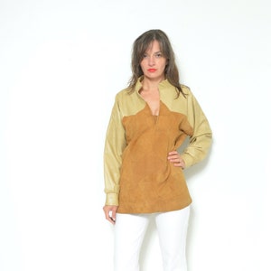 May include: A brown and beige suede and leather jacket with a V-neck and long sleeves. The jacket is worn by a person with white pants and red heeled sandals.