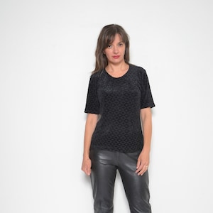 May include: A woman wearing a black quilted top and black leather pants. She is standing in front of a white wall and wearing brown heels.