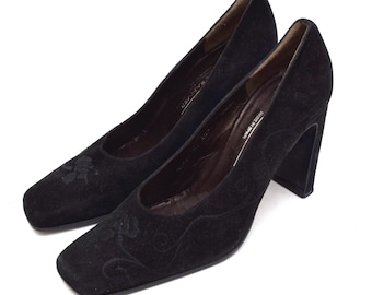 May include: Pair of black suede heeled pumps with a floral design. The heels are block heels.