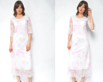 May include: A white maxi dress with a pink floral print and sheer sleeves. The dress has a ruffled hem and is worn with pink ankle boots.