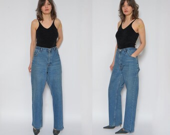 May include: A woman is wearing a black tank top and blue denim jeans. The jeans are a high-waisted, wide-leg style.