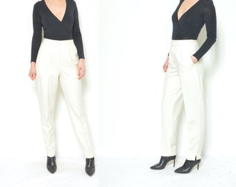 May include: A woman is wearing a black long-sleeved top with a deep V-neckline and white high-waisted pants. She is wearing black heeled shoes.