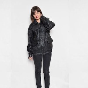 Puede incluir: Una chaqueta de cuero negra con cierre de cremallera y varios bolsillos. La chaqueta tiene un corte holgado y se combina con unos vaqueros negros.