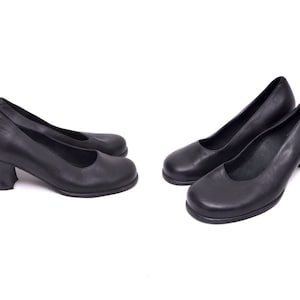 Może przedstawiać: Dwie pary czarnych skórzanych szpilek na niskim obcasie. Buty mają zaokrąglony nosek i zamknięty design.
