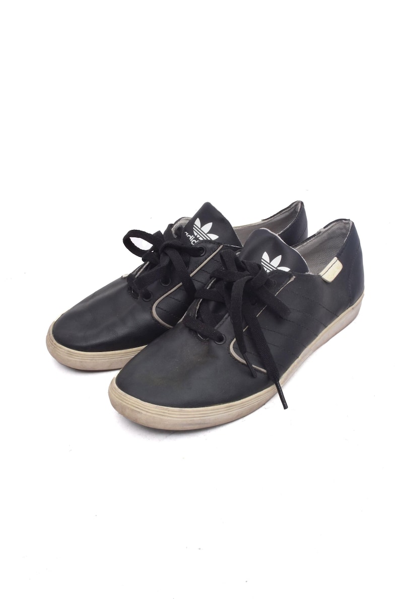 May include: A pair of black leather Adidas trainers with white laces and a white Adidas logo on the side.