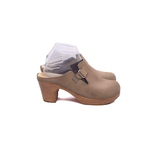Puede incluir: Zuecos de cuero color canela con tacones de madera. Los zuecos tienen punta redondeada, una correa con hebilla y suela de plataforma de madera. Los tacones miden unos 7.6 cm de alto.