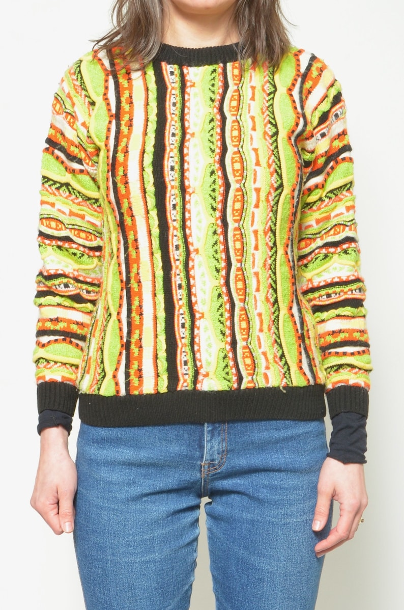 May include: A colorful striped sweater with a black crew neck. The sweater has a geometric pattern in shades of green, orange, black, and white.