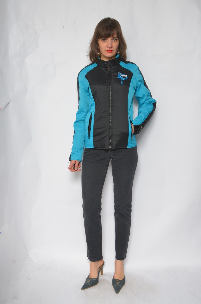 May include: A blue and black jacket with a zipper closure and a logo on the chest. The jacket has a sporty style.