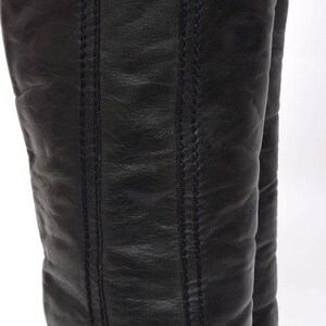 May include: A pair of black leather knee-high boots with a stitched seam detail on the back of the boots.