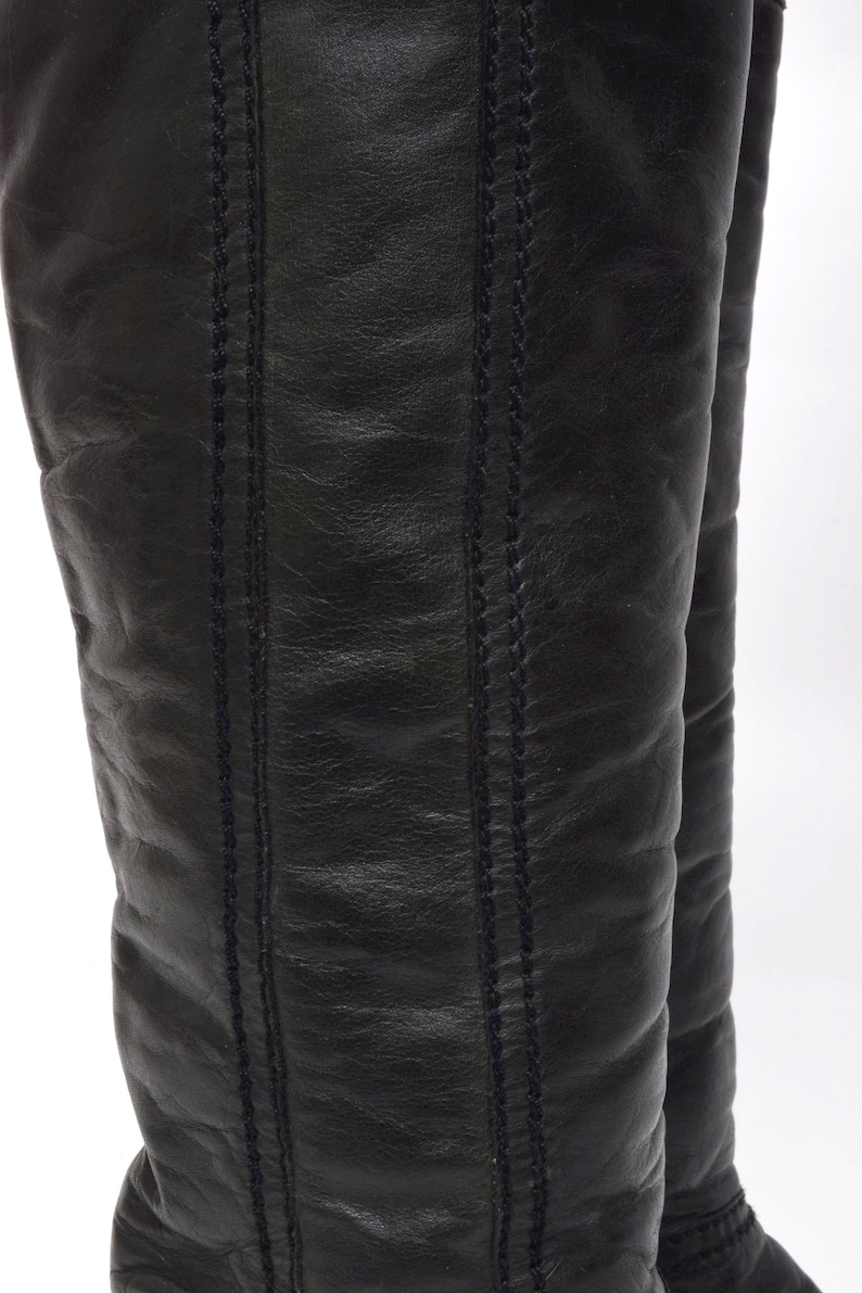 May include: A pair of black leather knee-high boots with a stitched seam detail on the back of the boots.
