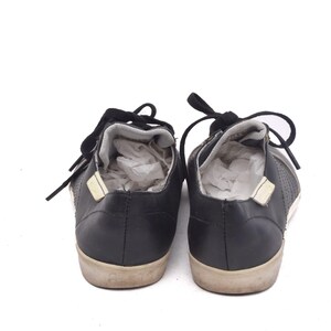 May include: A pair of black leather trainers with white laces. The trainers have a textured design on the sides and a white rubber sole.