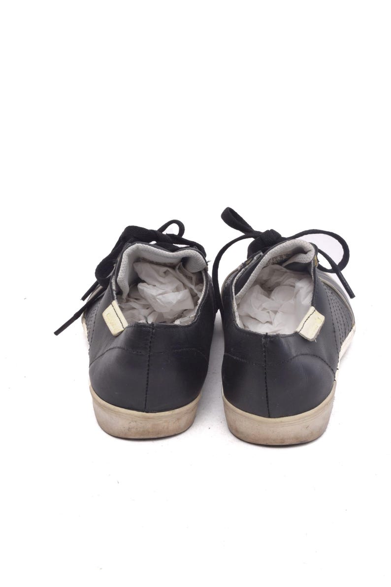 May include: A pair of black leather trainers with white laces. The trainers have a textured design on the sides and a white rubber sole.