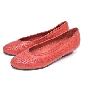 May include: A pair of coral-colored leather ballet flats. The toe box features a woven design, and the shoes have a low heel. The shoes are set against a white background.