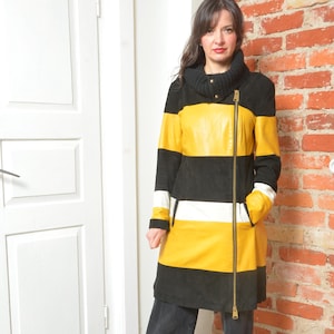 May include: A long, color-blocked coat featuring horizontal stripes of black, yellow, and white. The coat has a high, black collar, a full-length zipper, and a tailored fit. The sleeves are long, and the coat appears to be made of leather or a similar material.