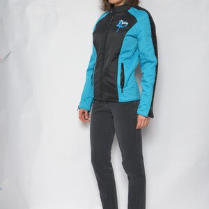May include: A black and blue jacket with a zipper closure and a logo on the left side. The jacket has a quilted design on the sleeves. The person is wearing black jeans and blue heeled shoes.
