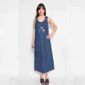 May include: A long denim dress with a sleeveless design and a scoop neck. The dress features three red and white stars with rhinestones on the front.