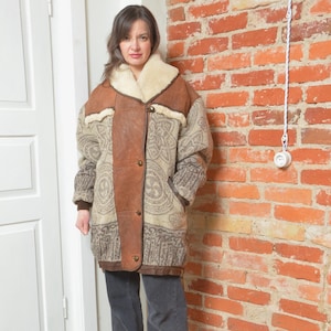 May include: A vintage brown and beige coat with a shearling collar. The coat features a paisley pattern on the body and brown leather accents. It has a button-up closure and pockets. The coat is a warm outerwear garment.