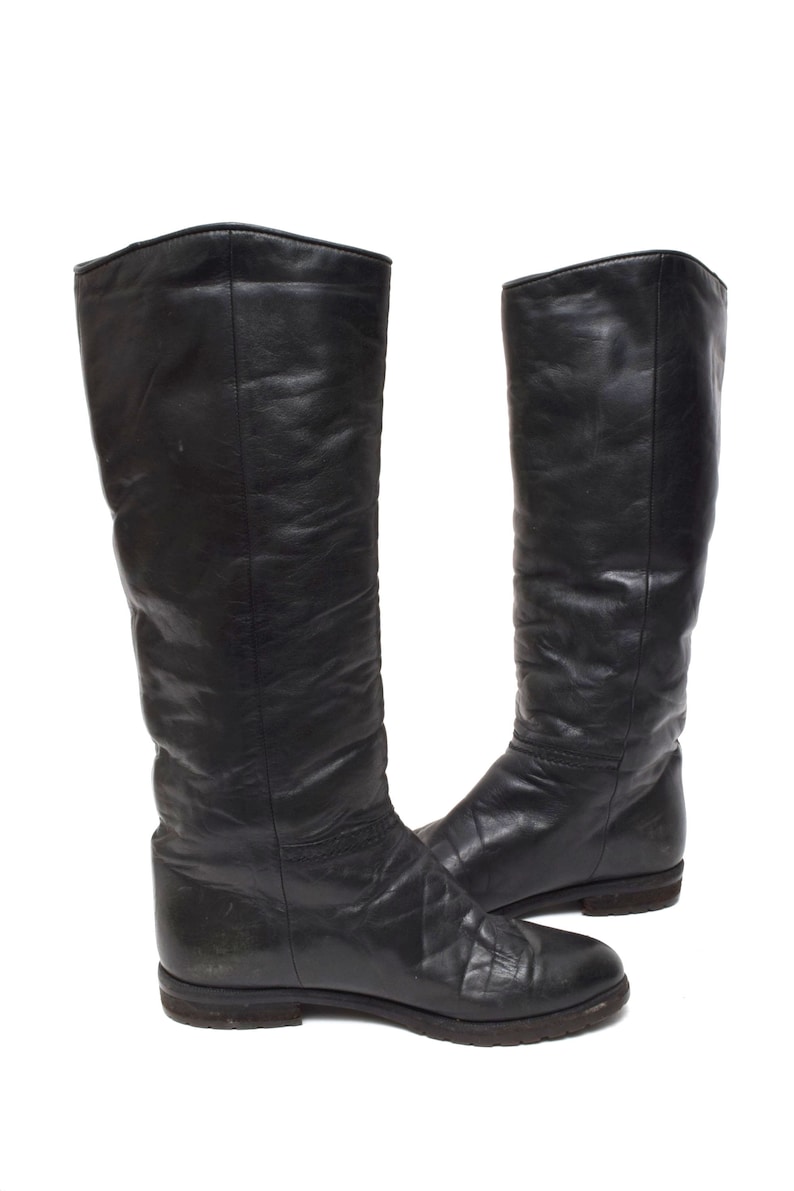 May include: A pair of black leather knee-high boots with a flat heel.