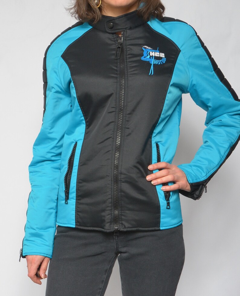 May include: A black and turquoise jacket with a zipper closure and a logo on the front that says "Hee Hotts".