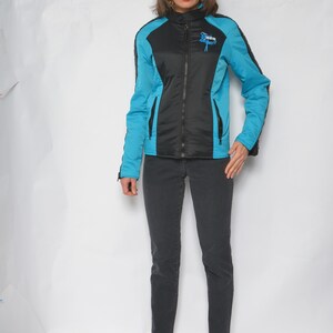 May include: A black and blue jacket with a zipper closure and a logo on the chest. The jacket is worn by a person with dark hair and is paired with black jeans and blue shoes.