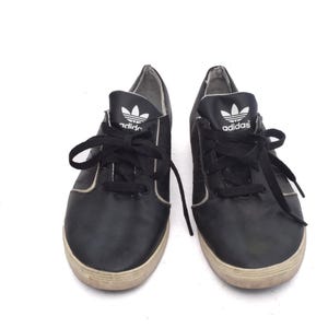 May include: A pair of black leather Adidas trainers with white laces and the Adidas logo on the side.