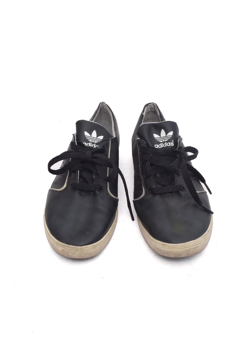 May include: A pair of black leather Adidas trainers with white laces and the Adidas logo on the side.