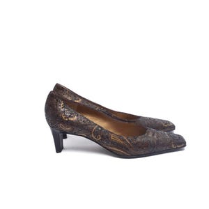 Könnte beinhalten: Ein Paar braune Pumps mit Paisley-Muster und kleinem Absatz. Die Schuhe haben eine spitze Zehenpartie und einen dunkelbraunen Absatz. Das Paisley-Muster enthält goldene und schwarze Akzente. Die Schuhe stehen vor weißem Hintergrund.