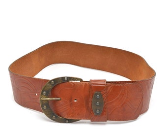 May include: A brown leather belt with an ornate metal buckle. The belt has a decorative embossed pattern.