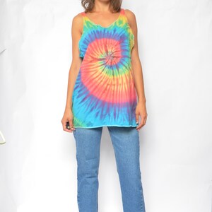 Puede incluir: Una mujer con un top de tirantes tie-dye con un patr&oacute;n de espiral arco&iacute;ris y pantalones vaqueros azules.